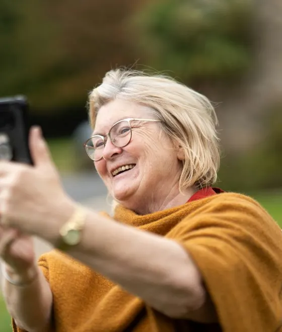A woman smiling as she takes a selfie with her phone